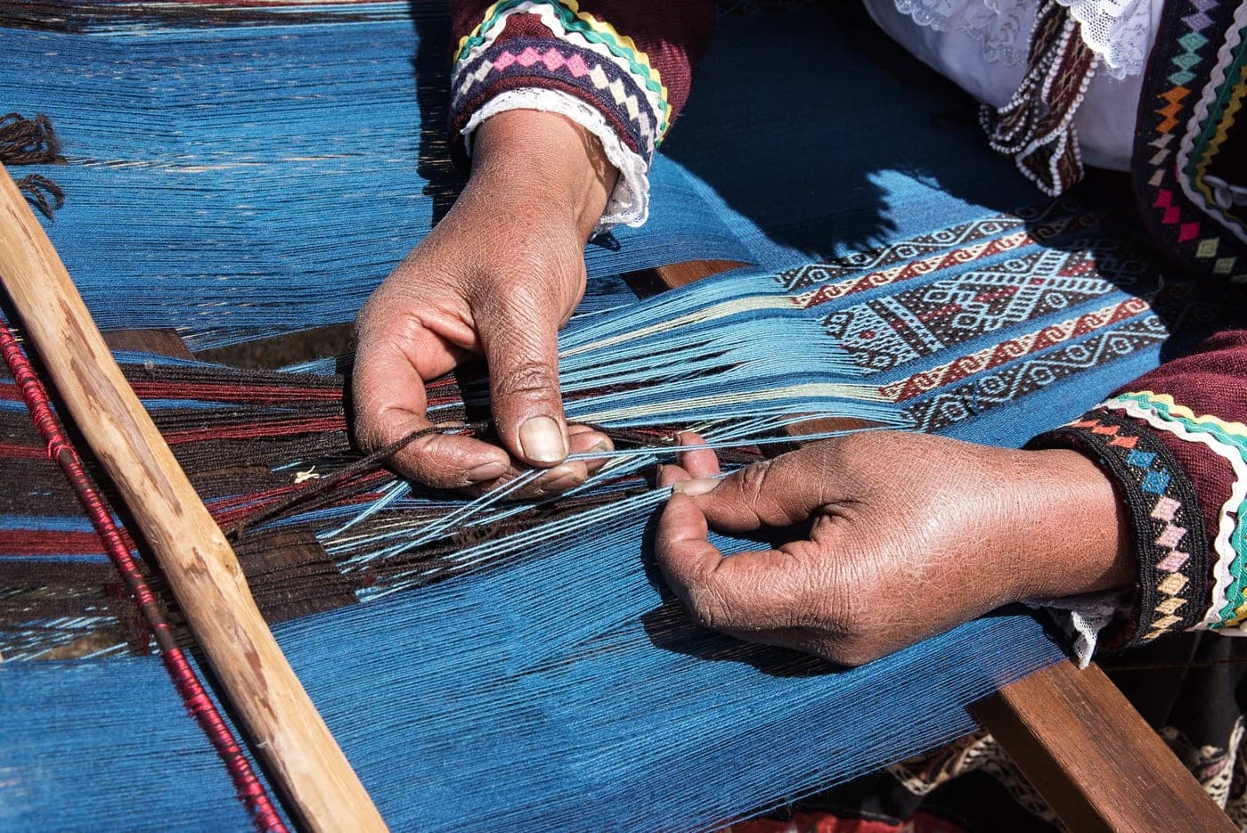 Hands weaving blue thread on a loom